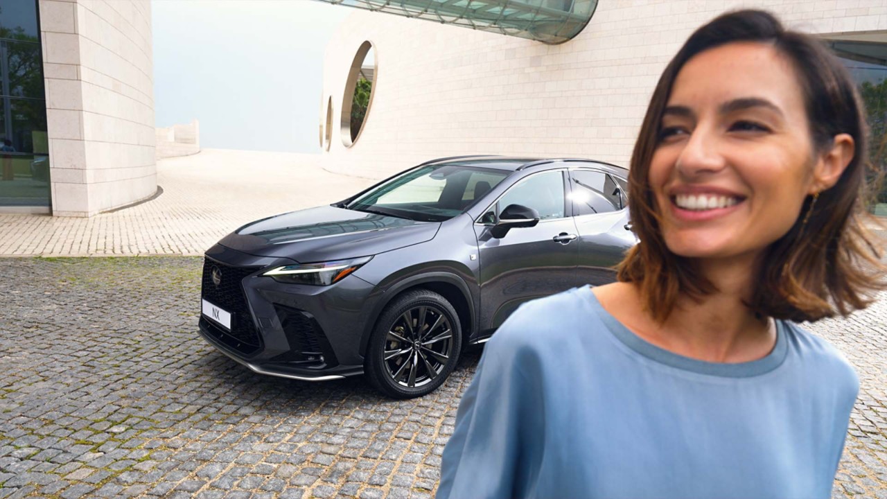 A smiling person walking away from a parked Lexus NX